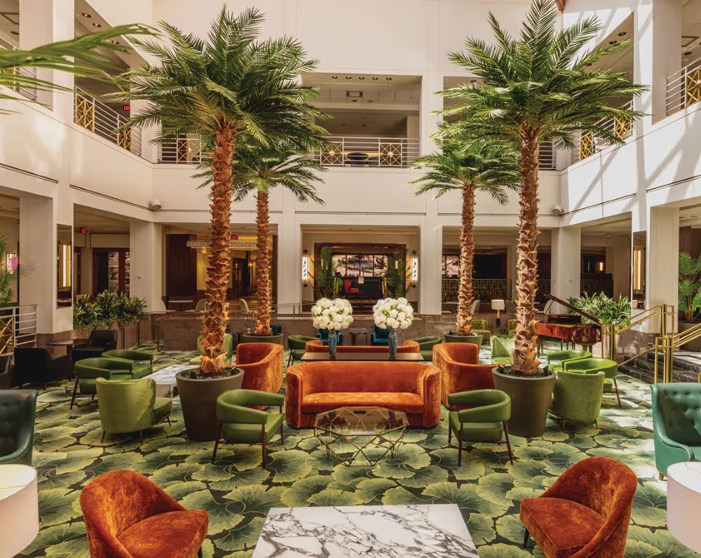 Lobby of the Clyde Hotel with palm trees and green chairs.